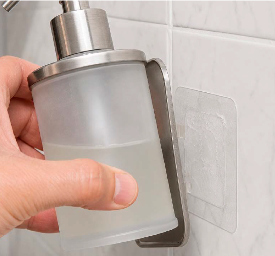 Soap dispenser mounted to bathroom tile with a pressure-sensitive adhesive strip.