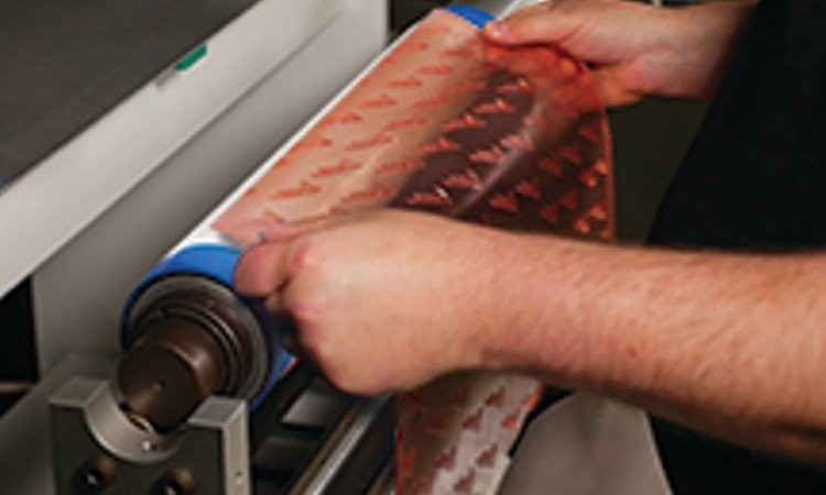 Photo  showing Avery Dennison Fas-Flex flexographic mounting tape being applied to a print roller by a pair of hands. 