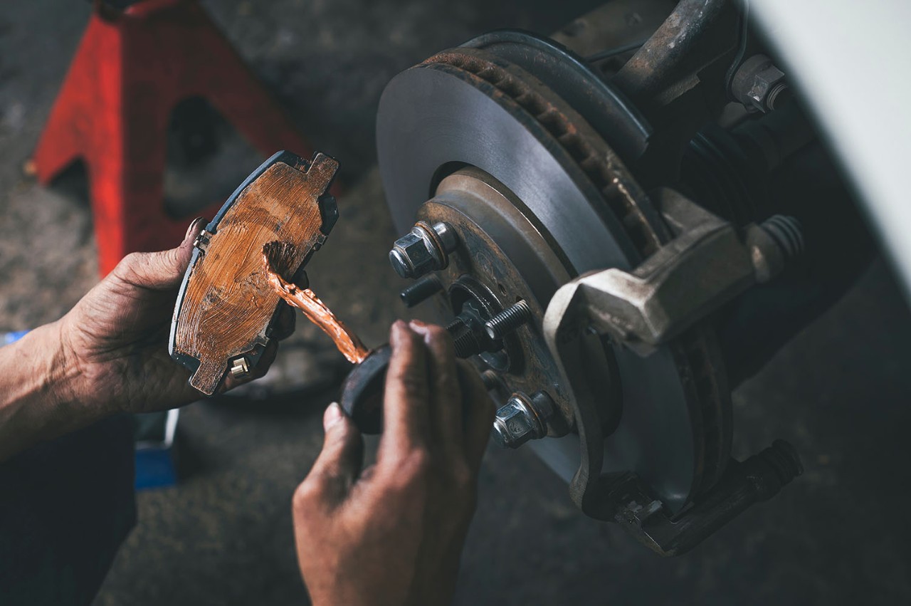 Photo showing a mechanic's hands working with a pair of brake pads. We offer adhesive tape products for brake shim vibration damping,