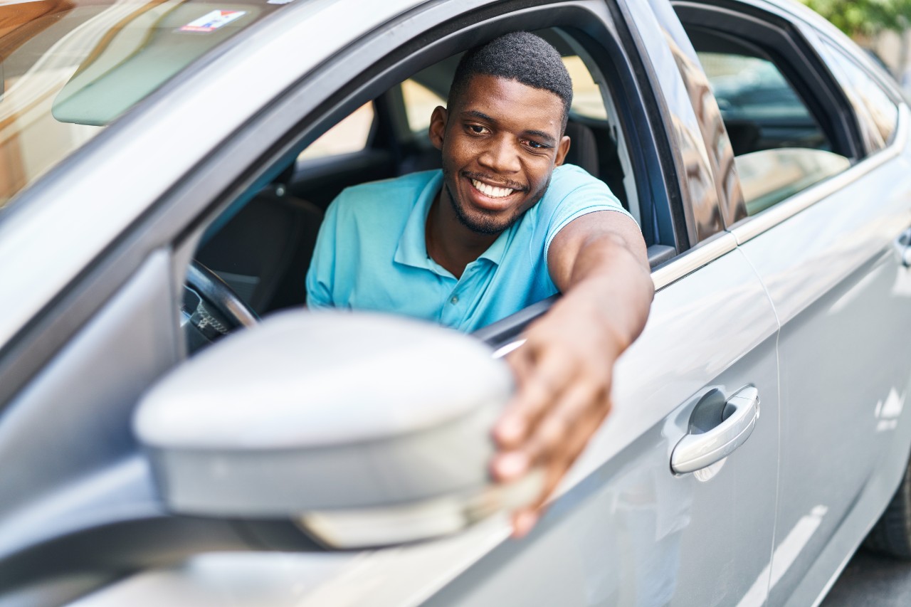 Photo of a driver adjusting their side-view mirror. Avery Dennison offers bonding solutions for mirrors and other vehicle components. 