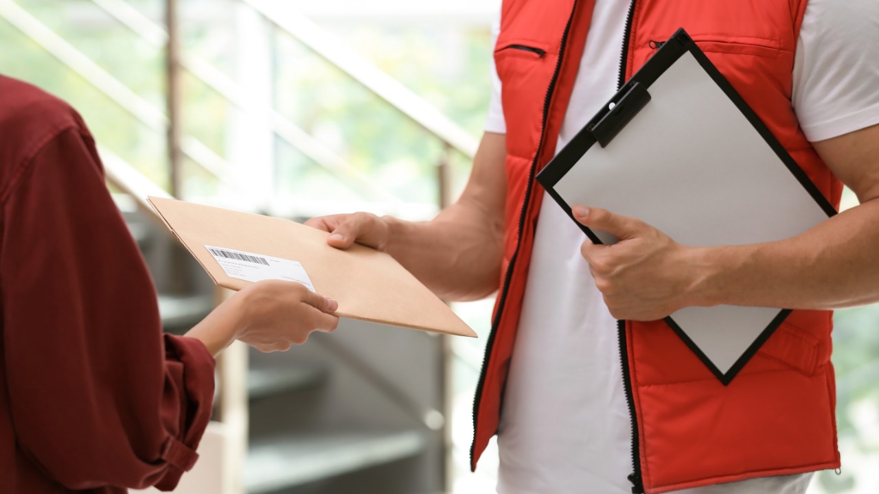 Photo closeup of a courier hand delivering a package that's been sealed with durable pressure-sensitive adhesive tape. 
